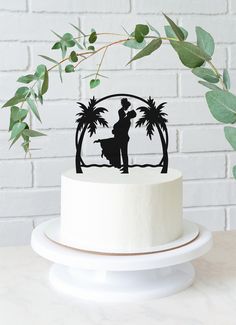 a white cake with a black silhouette of a man holding a surfboard and palm trees