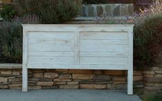 a white wooden bed sitting in front of a stone wall and plants on top of it