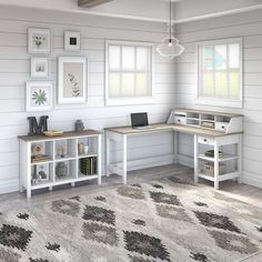 a computer desk sitting on top of a wooden floor next to a white rug and windows