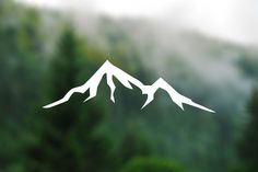 the mountains are covered in white paper cutouts on a glass surface with trees behind them