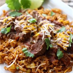 a white plate topped with rice covered in beef and cilantro sauce next to a lime wedge