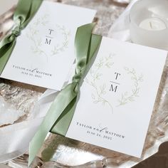 two cards with green ribbons tied to them on a silver platter next to a candle