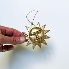 a hand holding a gold sun ornament with a face on it's side