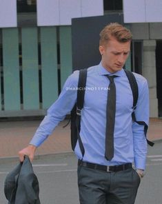 a man wearing a blue shirt and black tie walking down the street with a bag