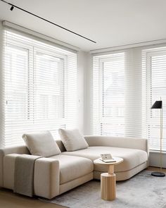 a living room filled with furniture and white blinds on the windows behind it is a round coffee table