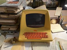 an old yellow computer sitting on top of a desk covered in books and papers,