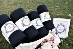 a basket filled with black towels next to flowers and framed pictures on the grass in front of it