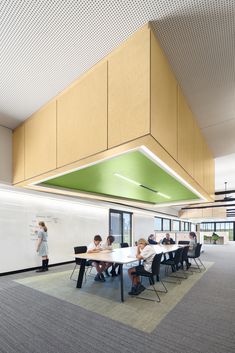 people are sitting at tables in an office setting with green accents on the ceiling and white walls