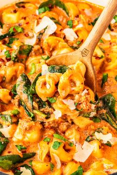 a wooden spoon in a pot filled with pasta and spinach