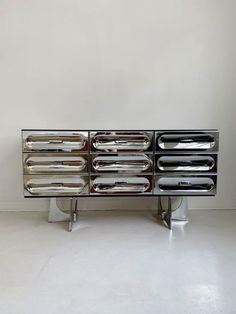 a silver metal cabinet with four drawers and chrome handles on each drawer, in front of a white wall