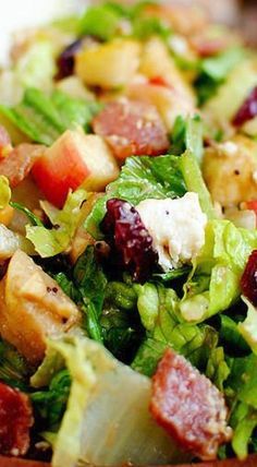 a salad with meat, lettuce and cranberries in a wooden bowl