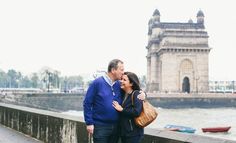 a man and woman standing next to each other on a bridge near the water with boats in the background