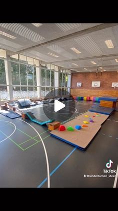 an indoor basketball court is shown with colorful balls on the floor and in front of large windows