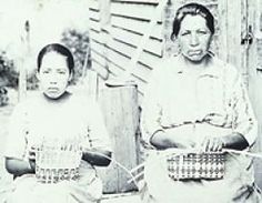 two women sitting next to each other in front of a house with baskets on their backs