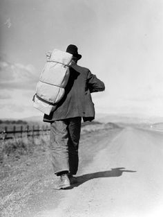 a man walking down the road with luggage on his back