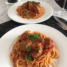 two white plates with spaghetti and meatballs on them