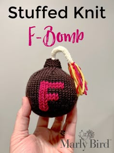 a hand holding a knitted ornament with the word f - bomb on it