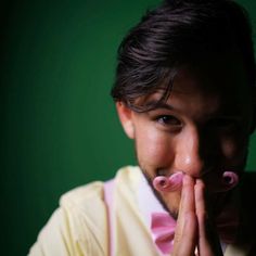 a man with his hands on his mouth and fingers in front of his face, wearing a pink bow tie