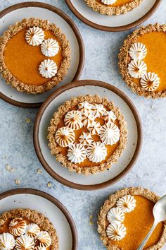 four pies with white frosting on them are arranged in small plates and one has a spoon