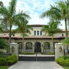 a gated driveway leading to a large house with palm trees in front of it