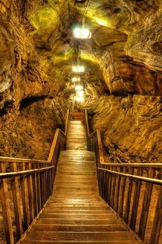 a wooden walkway leading to a cave with stairs going up it's sides and down the hill