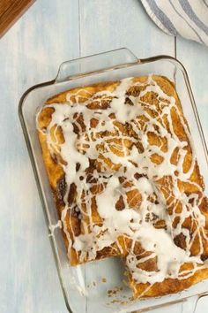 a pan filled with cinnamon rolls covered in white icing and drizzled