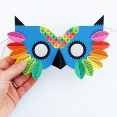 a hand holding a paper mask with colorful feathers on it