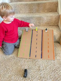 a little boy sitting on the floor playing with his toy cars and paper train set