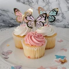 two cupcakes with pink frosting and butterflies on top are sitting on a plate