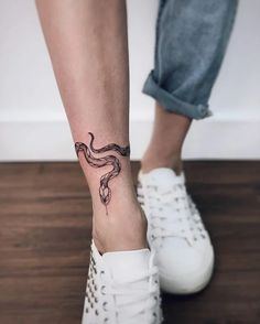 a woman's foot with a snake tattoo on her left ankle and white tennis shoes