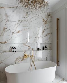 a white bath tub sitting under a chandelier next to a wall mounted toilet