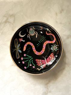 a black plate with colorful designs on it sitting on a white counter top next to a spoon