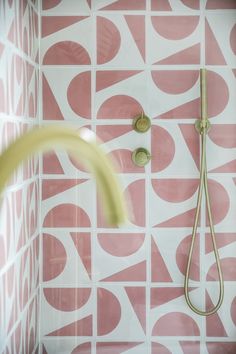 a pink and white tiled bathroom with a shower head, hand held shower faucet and soap dispenser