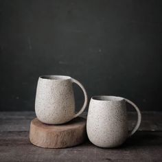 two white mugs sitting on top of a wooden table next to each other,