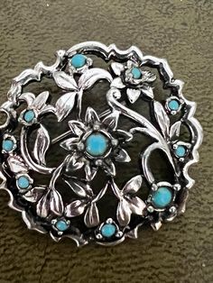 a silver brooch with blue stones on it's center and leaves in the middle