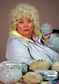 a woman sitting at a table with rocks on it and a stuffed animal in her hand