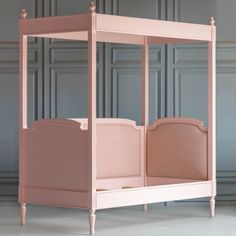 a pink canopy bed with wicker headboard and foot board on the floor in front of a blue wall