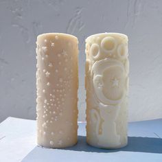 two candles sitting next to each other on top of a white tablecloth covered surface