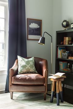 a living room with a chair, book shelf and lamp on the floor next to a window