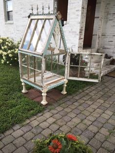 a small house made out of an old window pane and some flowers in the front yard