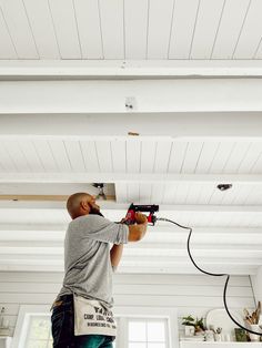 a man is using a power drill to paint the ceiling in his kitchen with white walls