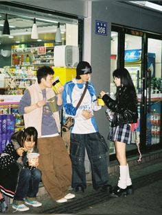 four people are standing on the sidewalk in front of a store with their cell phones