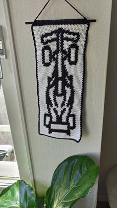 a crocheted sign hanging on the wall next to a potted green plant