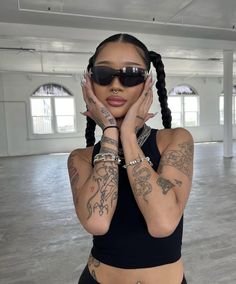 a woman with tattoos and sunglasses posing for the camera in an empty room wearing black