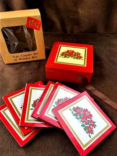 four red and gold cards in a wooden box with ribbon on the bottom, two are decorated with poinsettis