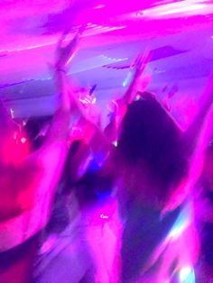 people dancing at a party with their arms in the air and lights on behind them