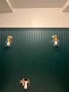 a bathroom with green walls and two lights on the wall above the toilet paper dispenser