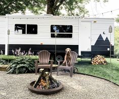 a dog sitting in front of a camper with chairs and fire pit on gravel