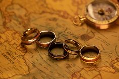 three gold wedding rings sitting on top of a world map next to a pocket watch