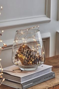 a glass bowl filled with pine cones and lights on top of a table next to a stack of books